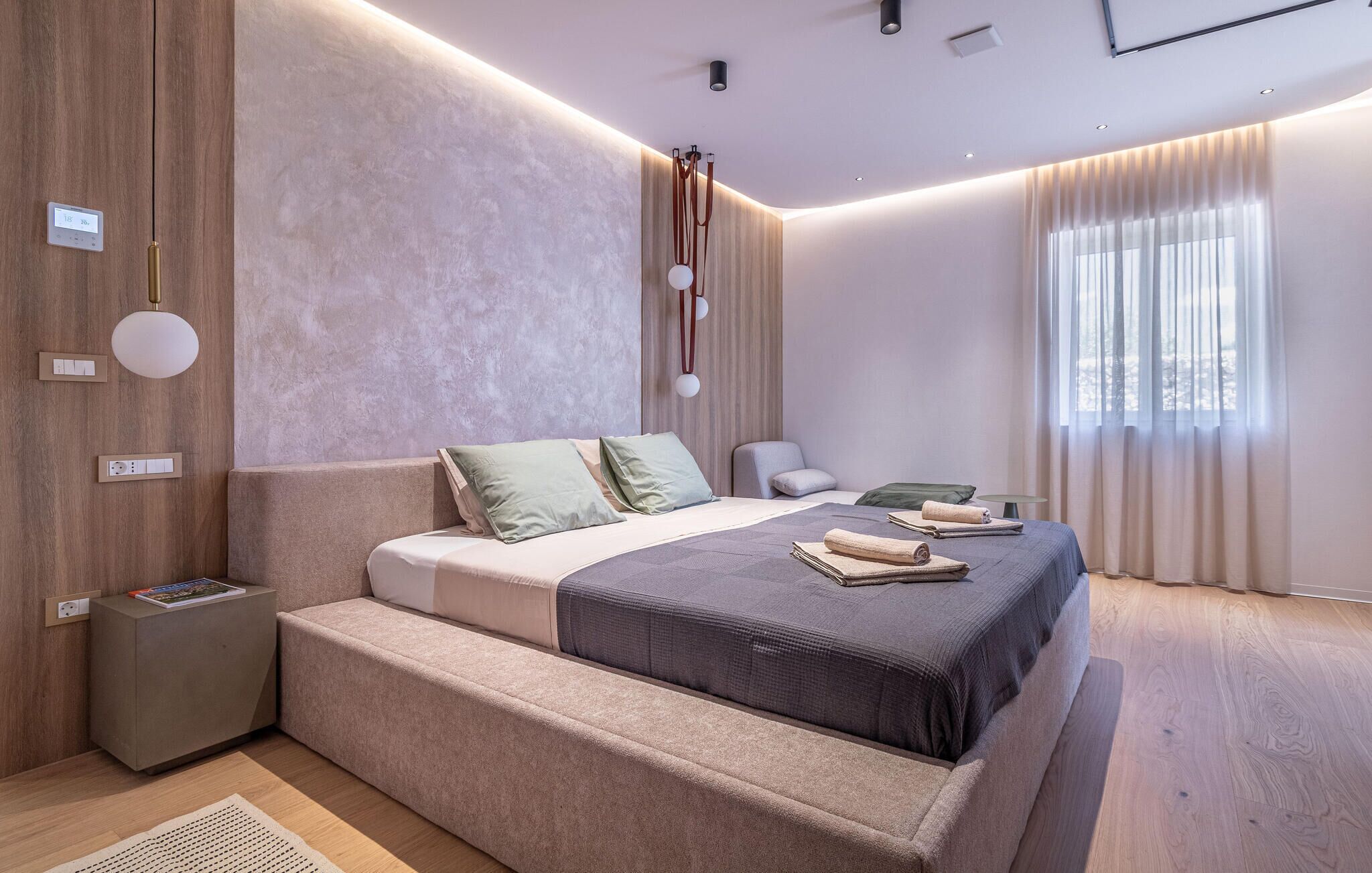 A modern bedroom with a large bed, bedside tables, a reading lamp, and a window with curtains.