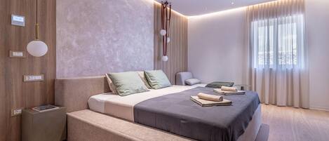 A modern bedroom with a large bed, bedside tables, a reading lamp, and a window with curtains.