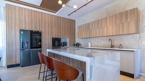 Une cuisine moderne avec des meubles en bois, un îlot central, des tabourets de bar et des appareils électroménagers intégrés.