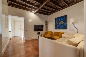 A modern living room with a wooden floor, a flat-screen TV, a sofa, two yellow armchairs, and a painting on the wall.