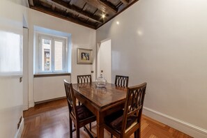A dining area with a wooden table and chairs, a window with blinds, and a framed picture on the wall.