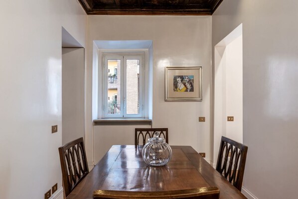 Un coin repas avec une table en bois, des chaises, une fenêtre avec des stores et un tableau encadré au mur.
