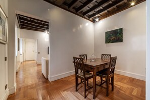 A dining area with a wooden table and chairs, a painting on the wall, and a hallway leading to another room.