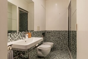 A modern bathroom with a white sink, two toilets, and a shower area.