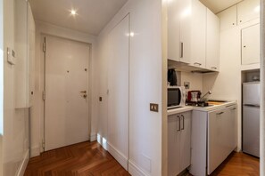 A compact kitchen with white cabinets, a microwave, a coffee maker, and a refrigerator.