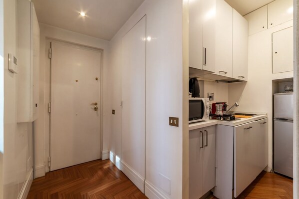 A compact kitchen with white cabinets, a microwave, a coffee maker, and a refrigerator.