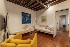 A modern living room with two white sofas, a yellow armchair, wooden flooring, and artwork on the walls.
