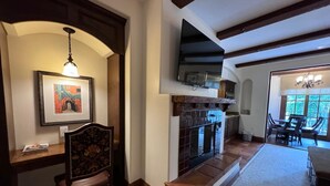 Un salon chaleureux avec une cheminée, un coin repas avec une table et des chaises, et une cuisine visible à travers une porte ouverte.