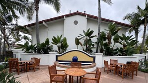 Un espace extérieur aménagé en terrasse, avec des tables et des chaises en bois, un mur décoratif recouvert de carreaux et une végétation tropicale luxuriante.