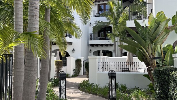 Un chemin mène à un bâtiment blanc doté de balcons, entouré de palmiers et de verdure.