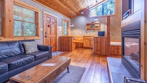 Ein gemütliches Blockhaus-Interieur mit Holzbalkendecke, einer Couch, einem Esstisch, einer Küchenzeile und einem Kamin.