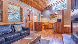 Ein gemütliches Blockhaus-Interieur mit Holzboden, einer Ledersofa, einem Esstisch und einer Küchenzeile mit Holzschränken und einem Fenster mit Blick auf den Wald.