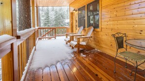 Eine Holzhütte mit einer Holzterrasse, zwei Adirondack-Stühlen, einem Metallstuhl und einem kleinen Tisch.