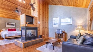 Ein gemütliches Blockhaus-Interieur mit Kamin, Holzwänden, einem Bett, einer Couch und gerahmten Bildern an der Wand.