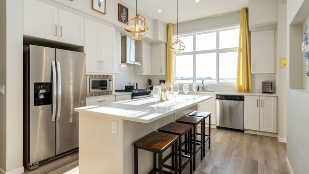 A modern kitchen with a central island, stainless steel appliances, and wooden stools.