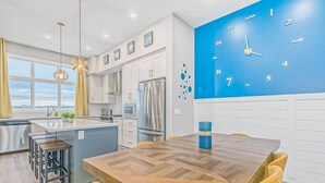 A modern kitchen with a blue wall clock, a large island, and a view of the outdoors.