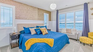A bedroom with a large bed, a nightstand, a chair, and a view of the water.
