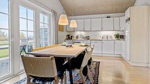 A modern kitchen with white cabinets, a wooden dining table, and a large window.