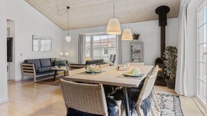 A modern living room with a wooden ceiling, a dining area with a table and chairs, a sofa, and a fireplace.