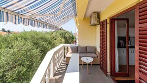 A balcony with a striped awning, a sofa, a small table, and a door leading to an interior space. - Awesome apartment in Bibinje with WiFi (Bibinje)