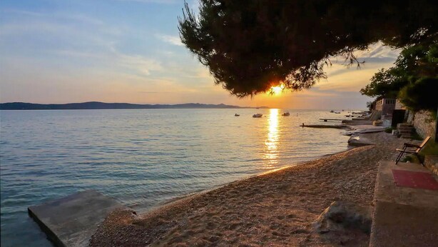 A beach with a sunset, calm water, and a row of benches along the shore. - Awesome apartment in Bibinje with WiFi (Bibinje)