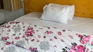 A bed with a yellow upholstered headboard, white bedding, and a floral-patterned duvet cover. - New Travellers Lodge (Lekki)