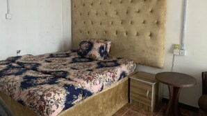 A bedroom with a large bed, a wooden nightstand, a small round table, and a headboard with tufting. - New Travellers Lodge (Lekki)