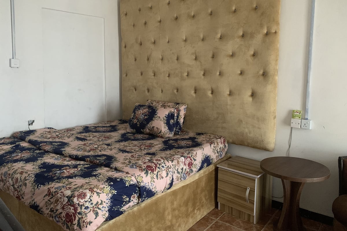 A bedroom with a large bed, a wooden nightstand, a small round table, and a headboard with tufting.