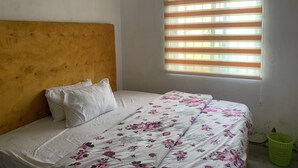 A room with a bed, a headboard, a window with blinds, and a green basket. - New Travellers Lodge (Lekki)