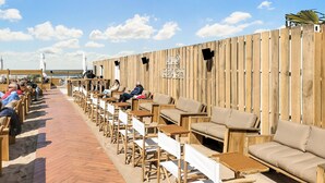 Un espace de détente aménagé au bord de la plage, avec des meubles en bois et un mur en bois sur lequel est inscrit le nom « LILO BEACH ».