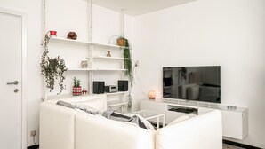Un salon moderne avec un canapé blanc, un téléviseur à écran plat et un meuble de rangement blanc équipé de haut-parleurs.