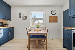 A modern kitchen with a wooden dining table, blue cabinets, and a window with a view.