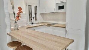 Una cocina moderna con armarios blancos, encimera de madera, microondas integrado y un florero con flores en la encimera.