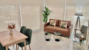Una sala de estar moderna con un sofá, dos mesas auxiliares, una lámpara y una mesa de comedor con sillas.