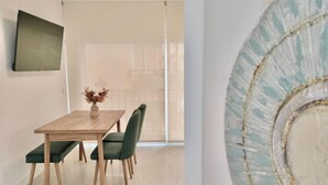 Un área de comedor con una mesa de madera, sillas tapizadas de color verde y un jarrón con flores secas.