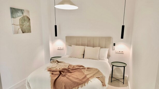 Un dormitorio moderno con una cama grande, dos mesitas de noche, una lámpara colgante y un cuadro en la pared.