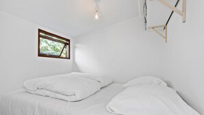 Ett enkelt, vitt rum med en säng, ett litet fönster och en hängande lampa.