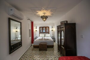 Quarto de hotel com uma cama grande, cômoda, espelho e um candelabro.