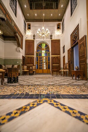A spacious room with a patterned floor, wooden furniture, and a large arched doorway. - Dar Usham Fes (Fes)