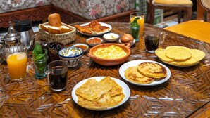 Un área de comedor tradicional marroquí con una mesa estampada, un sofá con tapicería floral y una puerta de madera.