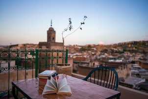 Uma mesa com livros e vista para a cidade, com uma torre imponente ao fundo.