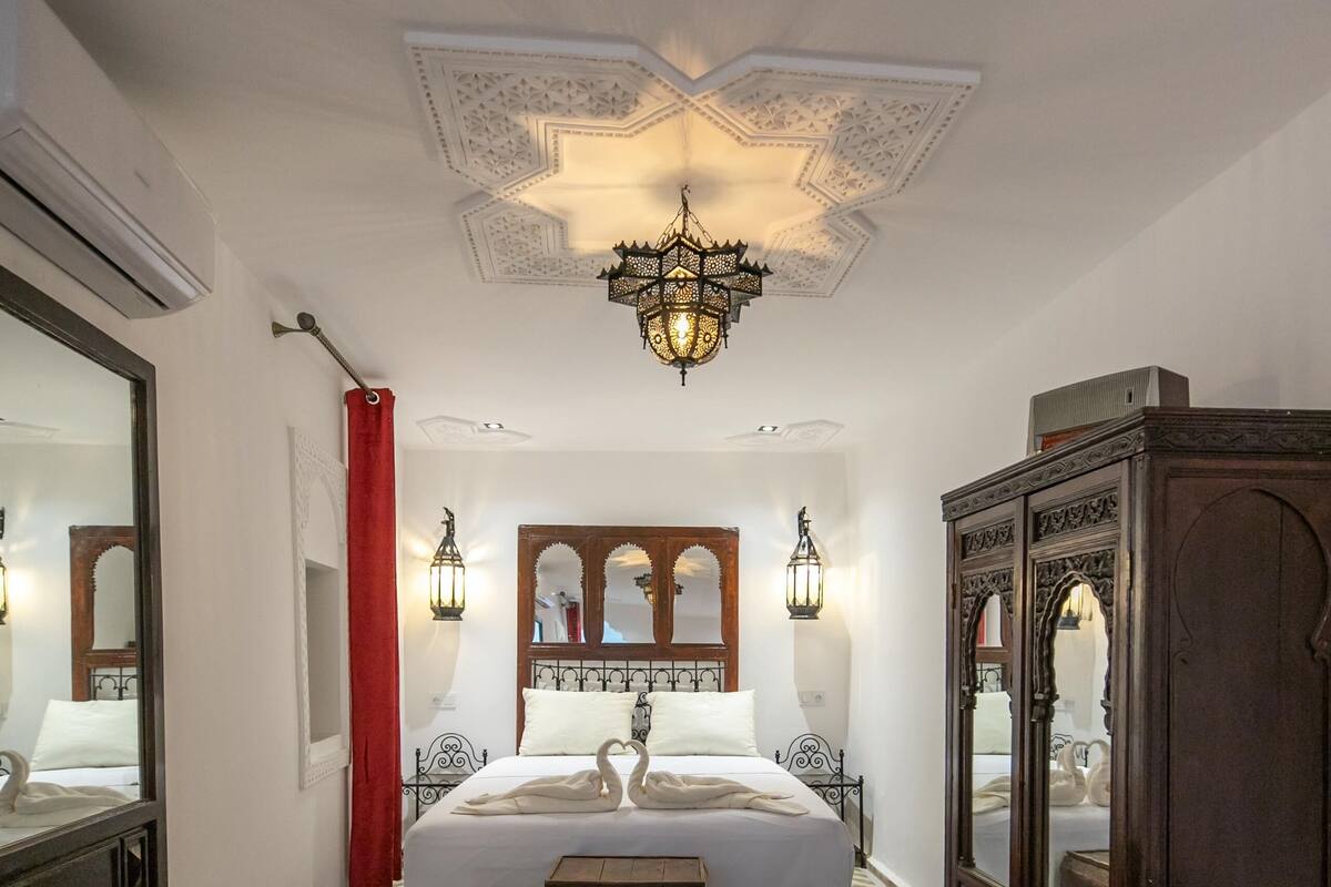 A bedroom with a bed, a mirror, a wardrobe, and a patterned rug.