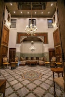 Um interior tradicional marroquino com mobiliário de madeira ornamentado, um chão estampado e um candelabro.