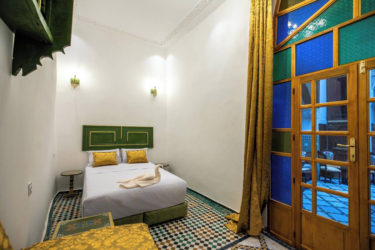 A hotel room with a bed, a small table, and a view through a wooden door.