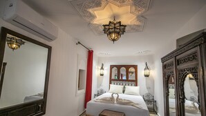 Habitación de hotel con una cama grande, techo ornamentado y espejos decorativos.