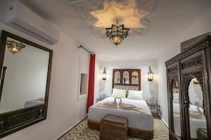 Quarto de hotel com uma cama grande, teto ornamentado e espelhos decorativos.