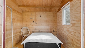 Une petite pièce en bois, aménagée comme une cabane, avec un lit, une chaise et une fenêtre.