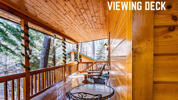 A wooden cabin with a viewing deck featuring a round table and chairs, surrounded by wooden railings and large windows. - Romantic Cabin | River Sounds | Hiking (Ruidoso)