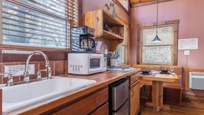 A kitchen with wooden cabinets, a white sink, a microwave, and a dining area with a wooden table and chairs. - Romantic Cabin | River Sounds | Hiking (Ruidoso)