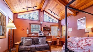 A cozy cabin interior with a wooden ceiling, a sofa, a bed, and a desk area. - Romantic Cabin | River Sounds | Hiking (Ruidoso)